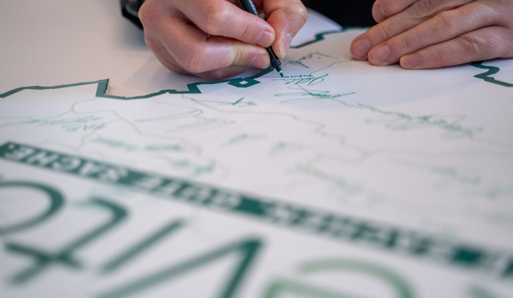 Auf dem Bild ist eine Niederösterreichkarte mit dem ReVital Logo zusehen sowie die diverse Unterschriften und eine Hand, die einen grünen Stift hält und unterschreibt.