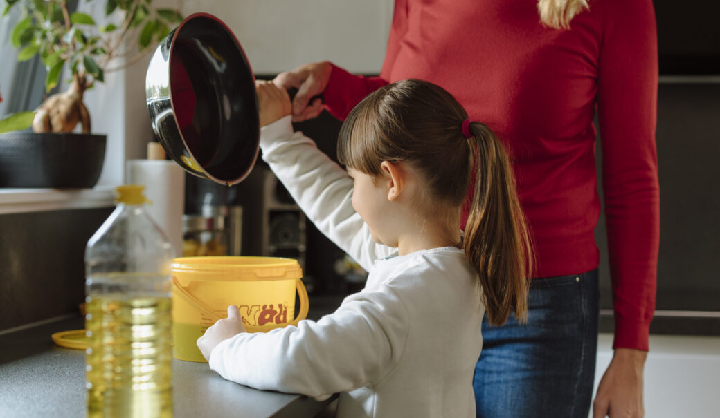 Das Bild zeigt eine Mutter mit ihrer Tochter, die gebrauchtes Speise&ouml;l in einen gelben Beh&auml;lter umf&uuml;llen.