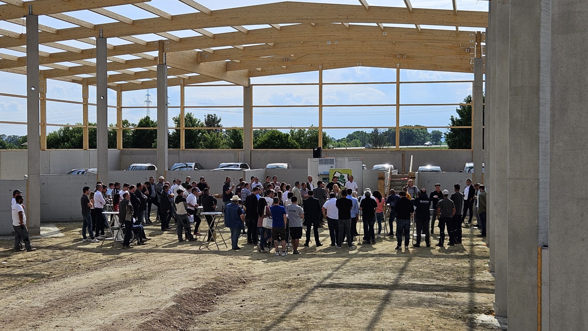 Gleichenfeier im Wertstoffzentrum. Zu sehen sind viele Menschen, die auf der Baustelle des WSZ unter dem offenen Dachstuhl stehen.