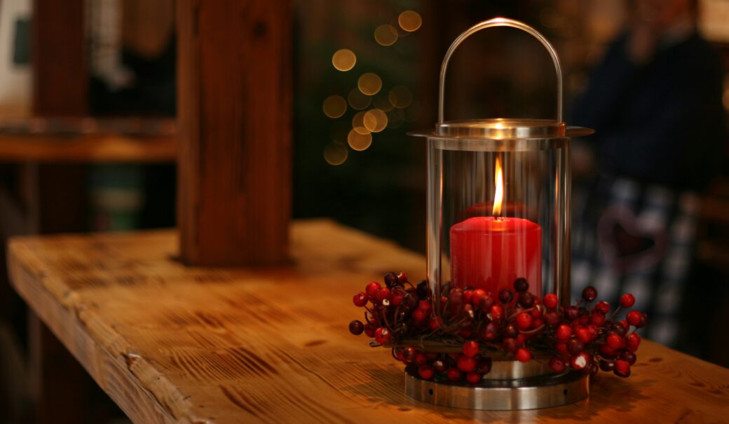 Das Bild zeigt einen Tisch mit einer roten Kerze in einem Windlicht.